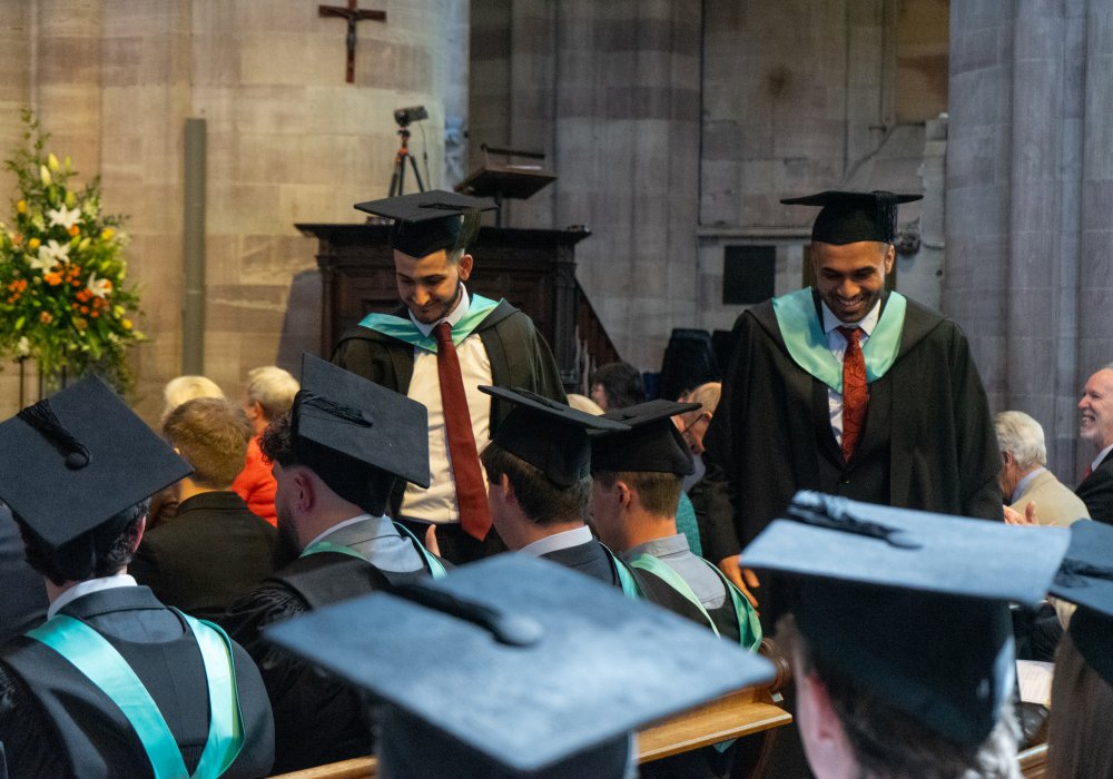 Two Students in graduate robes walking through the Hereford Cathedral