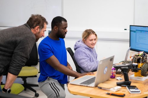 Two NMITE students working on a computer alongside one of NMITE's academic team