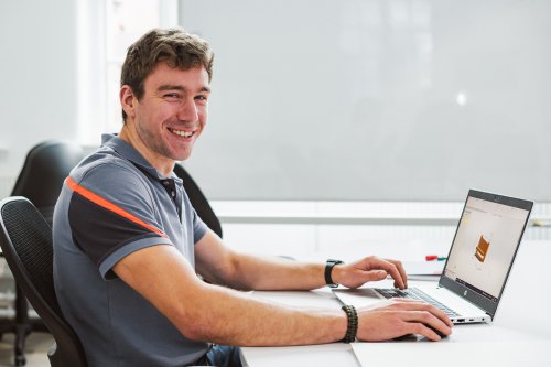 Male student smiling whilst sat at his laptop in an NMITE studio