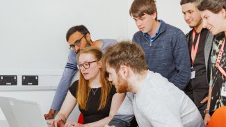 A group of NMITE students working together on a challenge around a laptop.
