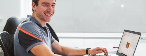 Male student smiling whilst sat at his laptop in an NMITE studio