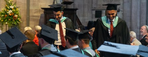 Two Students in graduate robes walking through the Hereford Cathedral